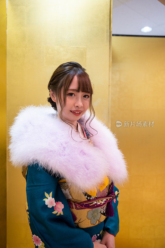 在“Seijin Shiki”成人礼上，年轻女子身着Furisode和服和毛皮领披肩站在金色的“Byobu”折叠屏风前